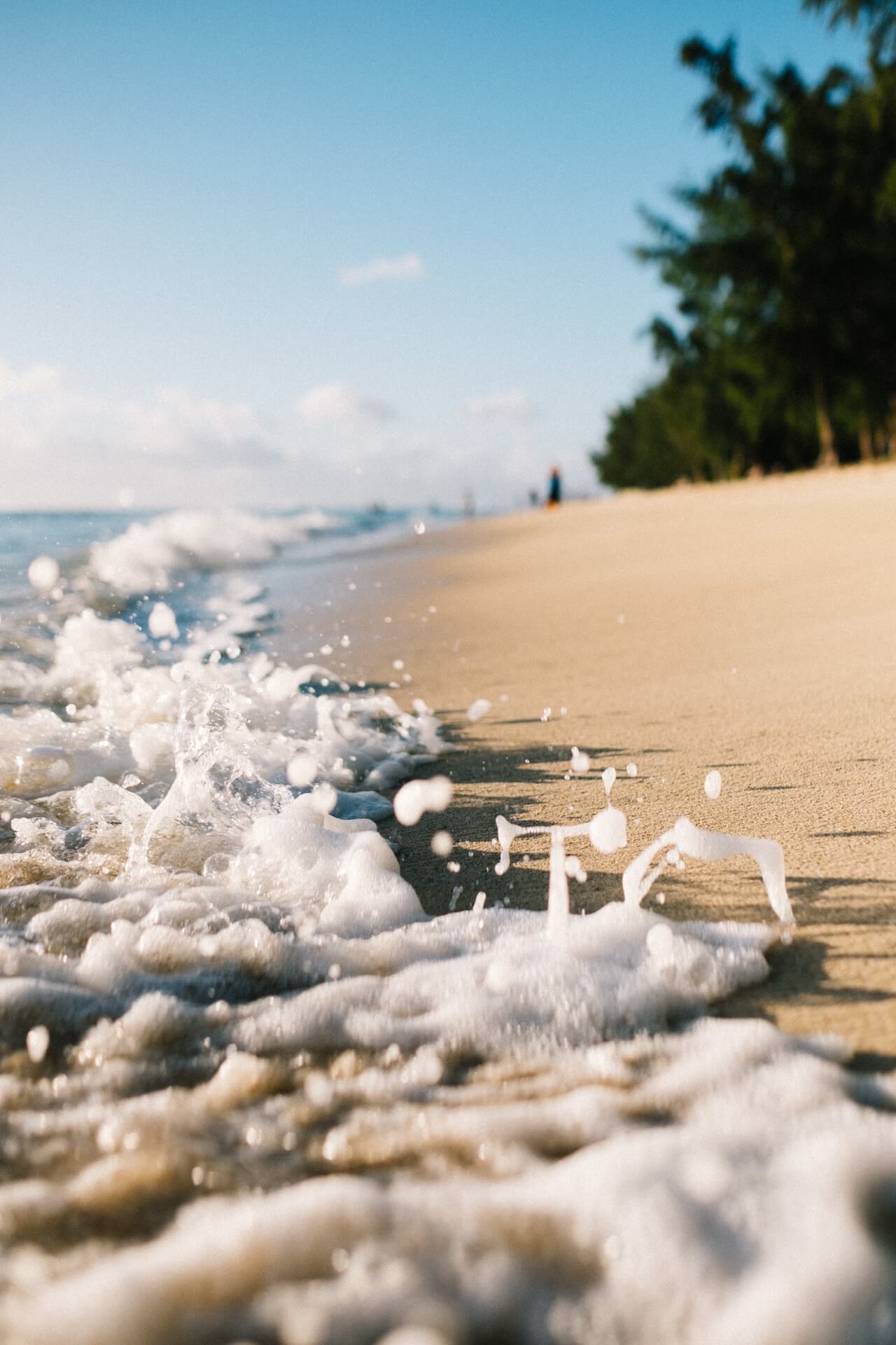 Very small wave crashing on a perfect golden sand beach