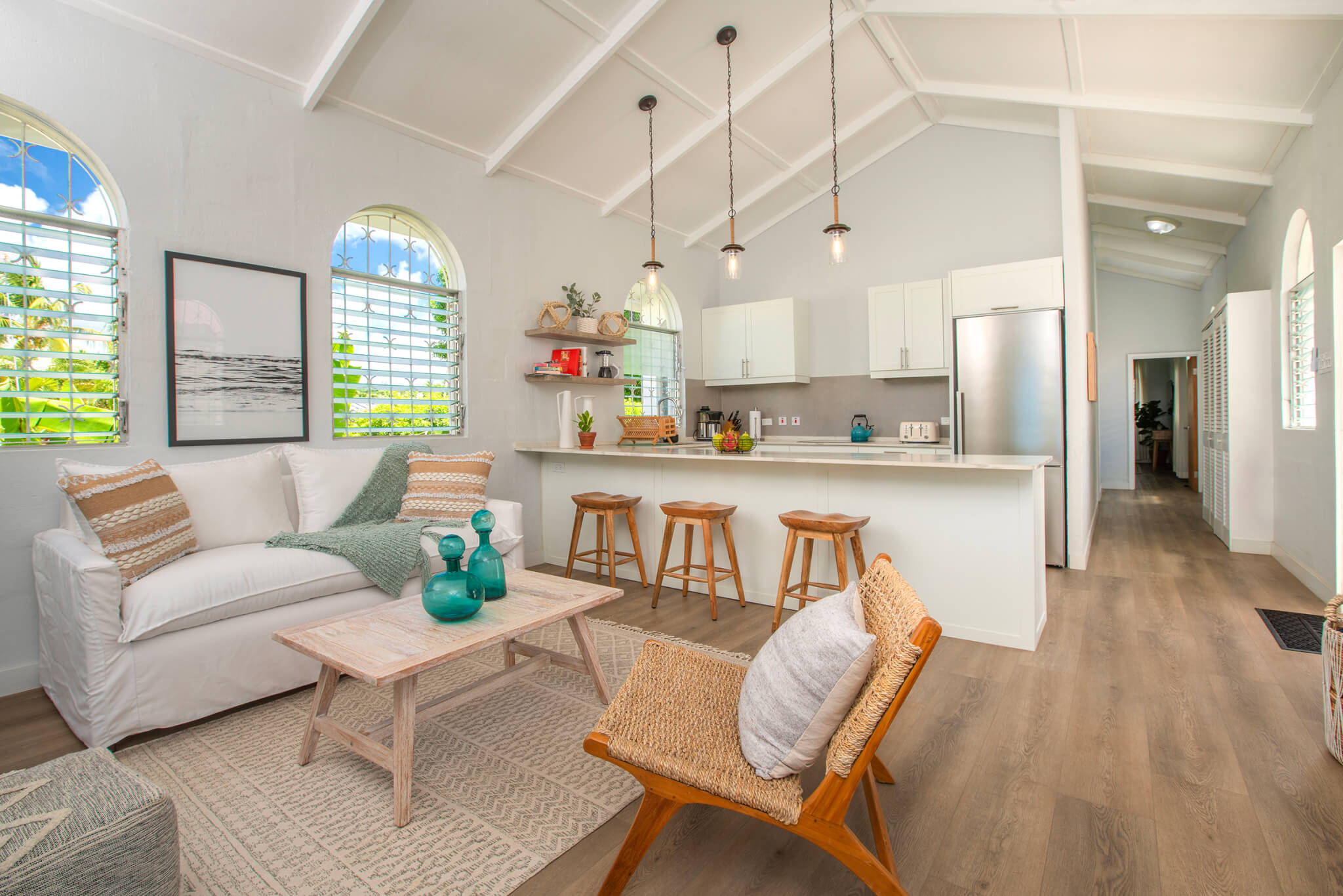 Open plan lounge and kitchen with hanging light features above the breakfast bar that separates the two spaces